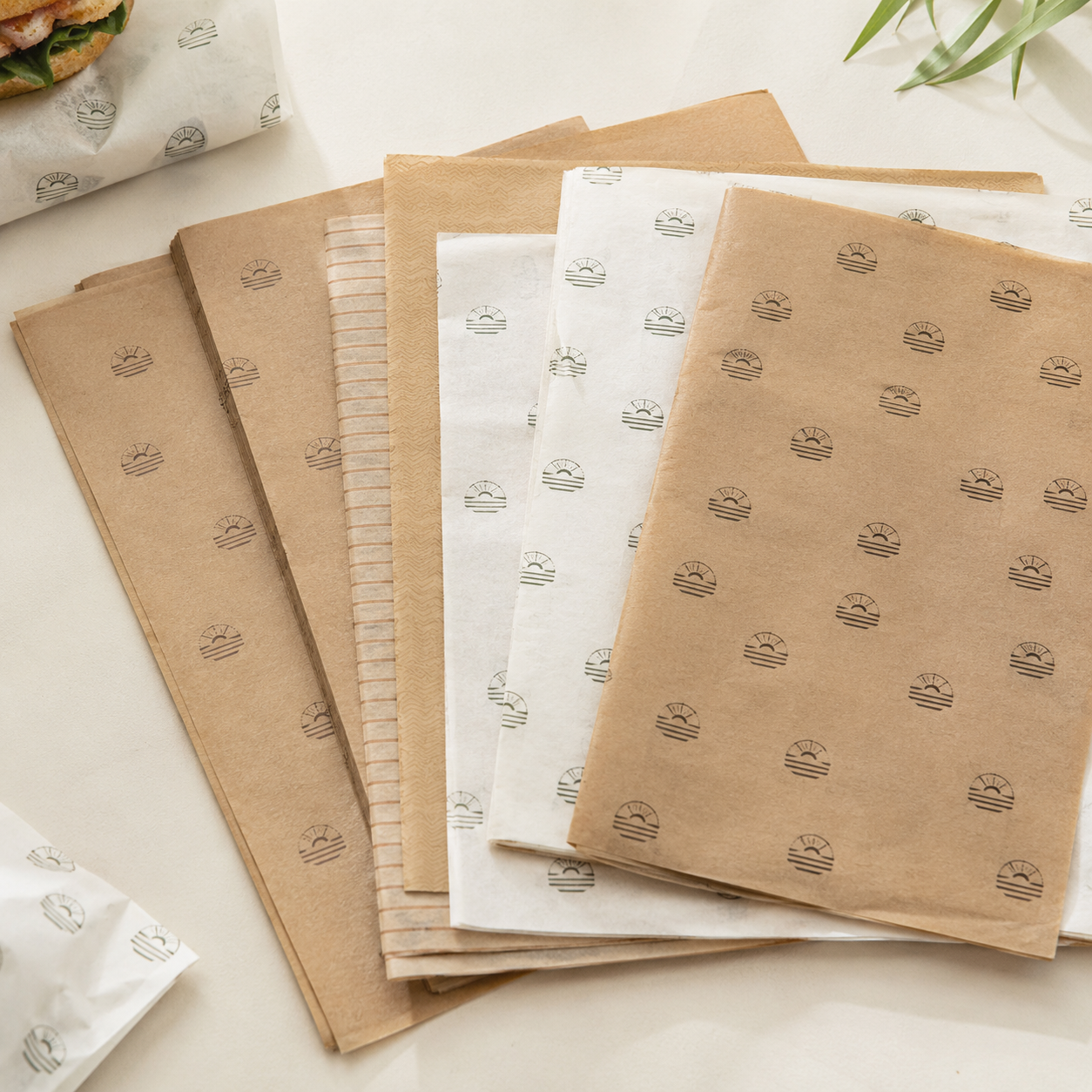 Stack of custom-printed greaseproof paper sheets fanned out on a light countertop, showing a subtle repeating stamp pattern